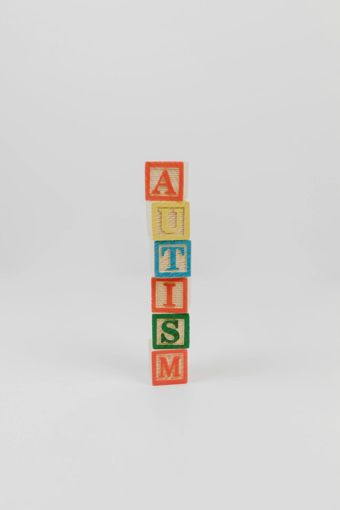 Vertical stack of colorful wooden blocks spelling 'AUTISM' on a white background.